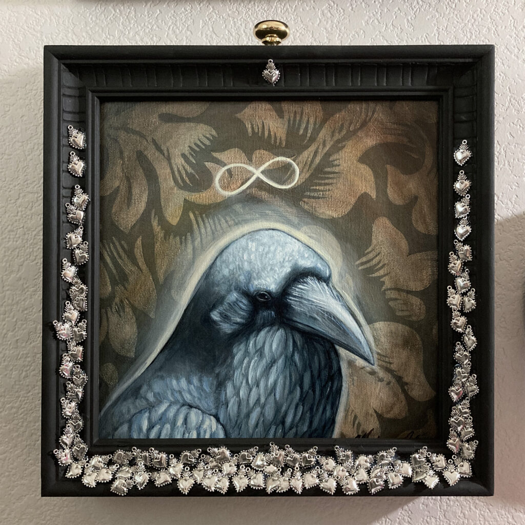 Raven the Elder mixed media artwork. Painting portrait of a raven with the infinity symbol above it's head. In a frame with silver sacred heart charms attached to the front.